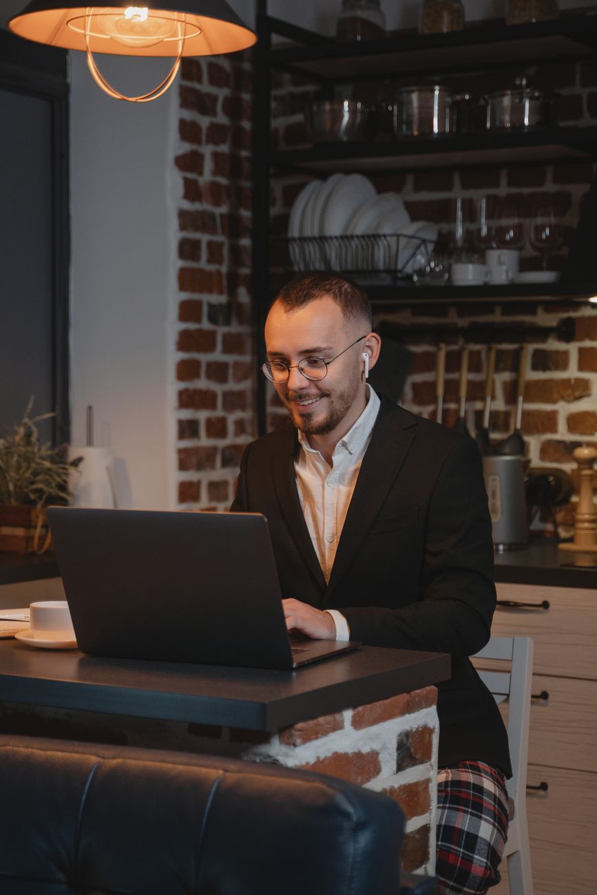 A man in headphones talks to his laptop in a kitchen