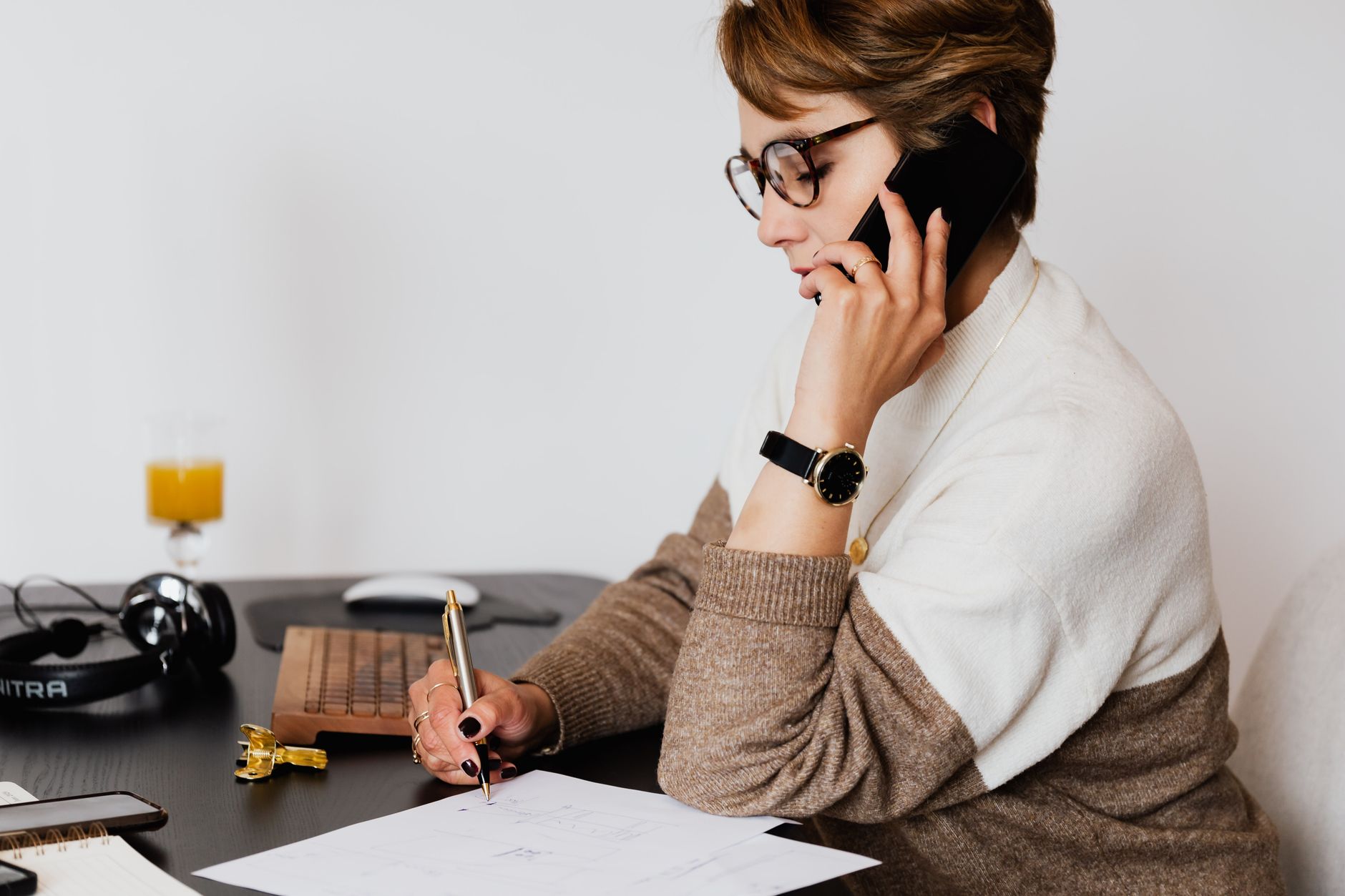 A woman on a phone call writes notes at her desk